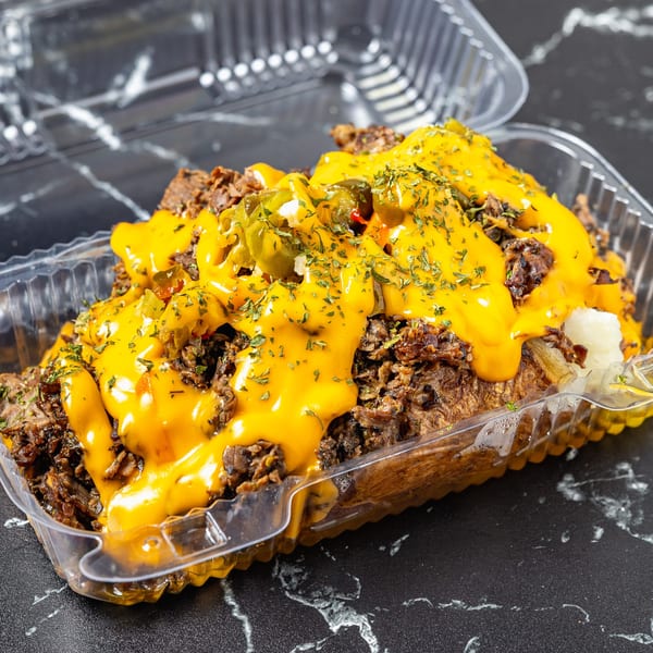 A Watta Potato by Yogis Bistro, loaded with shredded meat, melted cheese, and jalapeños in a plastic container.