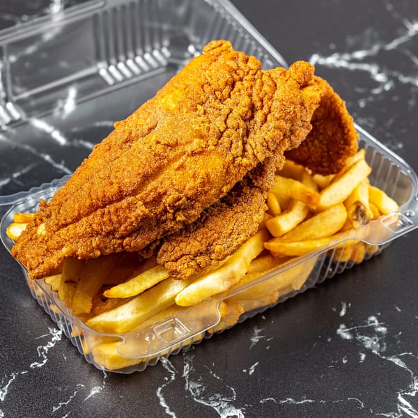 Crispy fried fish fillets and golden french fries in a clear plastic takeout container on a dark marble surface.